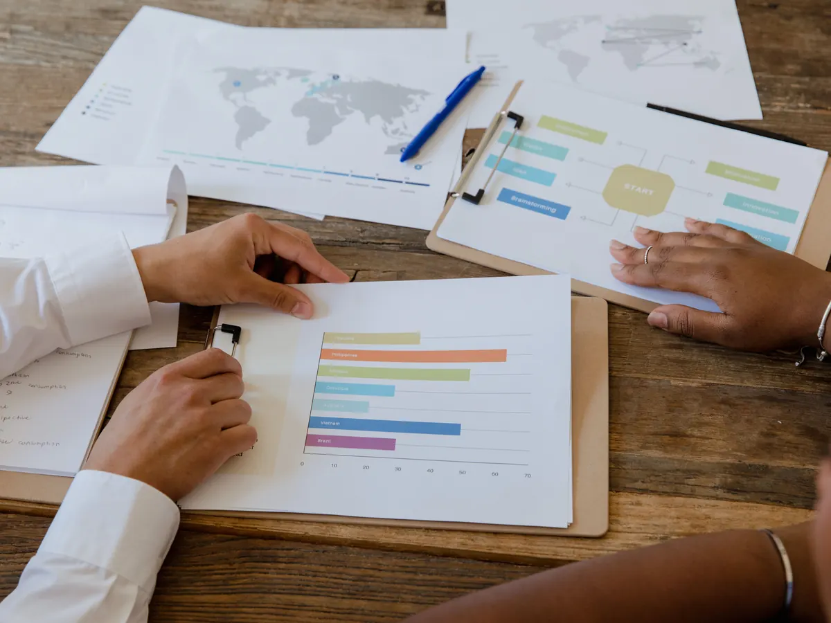 Reviewing SEO and web development case studies: two people’s hands on a printed bar chart and project notes on a wooden desk