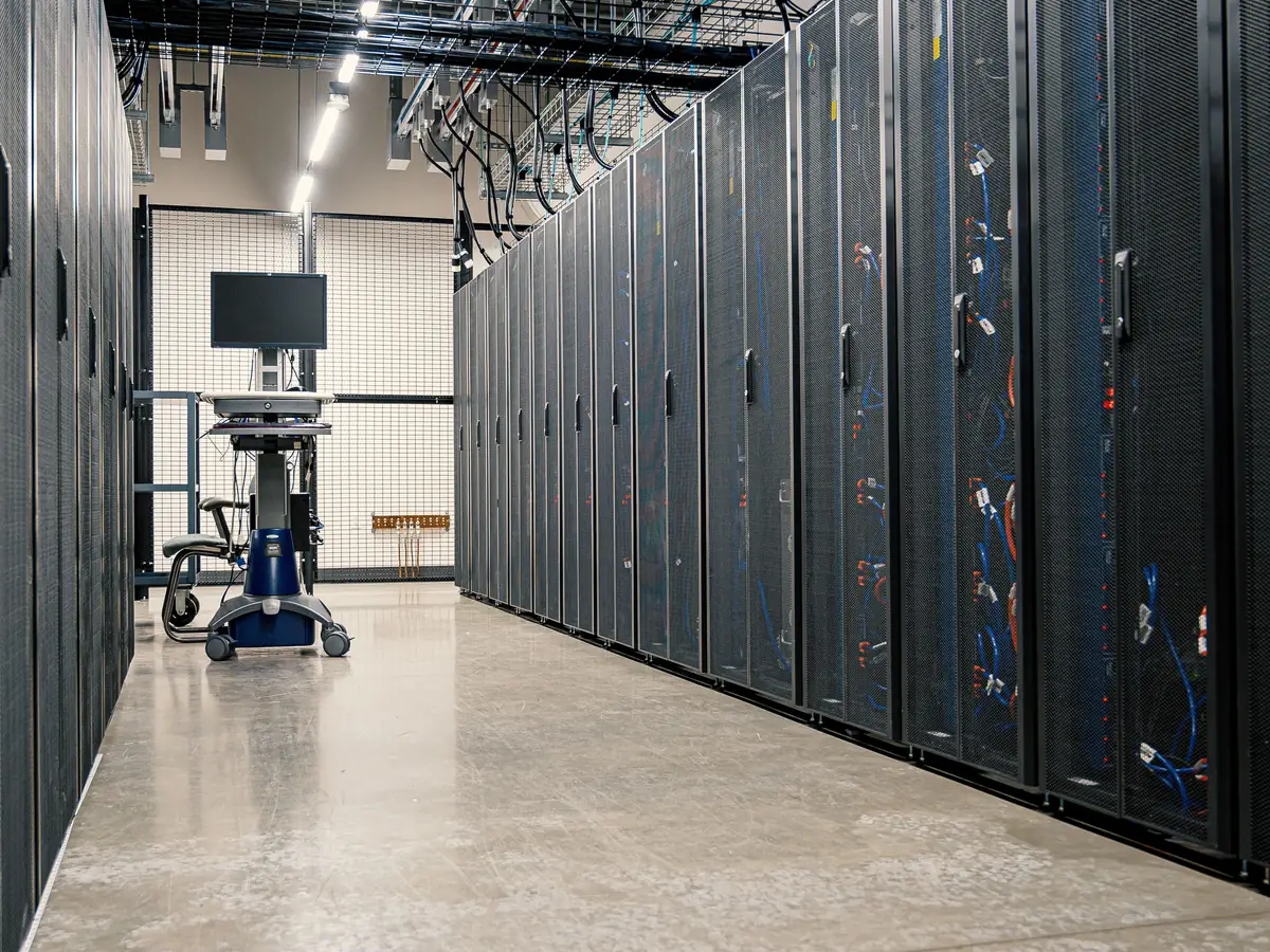 Aisle of black server racks with blue and orange network cabling in a clean, well-lit data center
