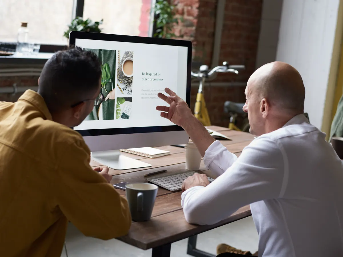 Two colleagues discussing a website layout on a desktop monitor in a studio office