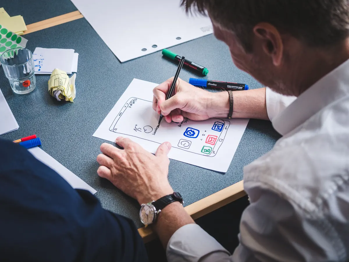 Designer sketching a mobile app screen with colored icons on paper during a wireframing session