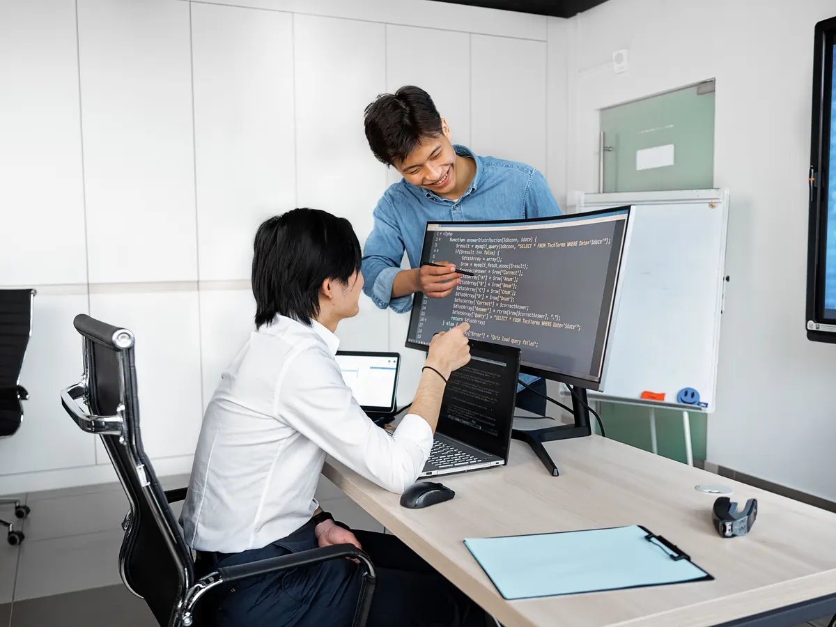 Two developers reviewing code together on a curved monitor during a website and software development project