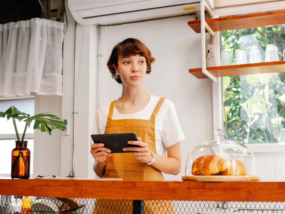 Cafe owner holding a tablet behind her bakery counter, the kind of local business our local SEO services help nearby customers find
