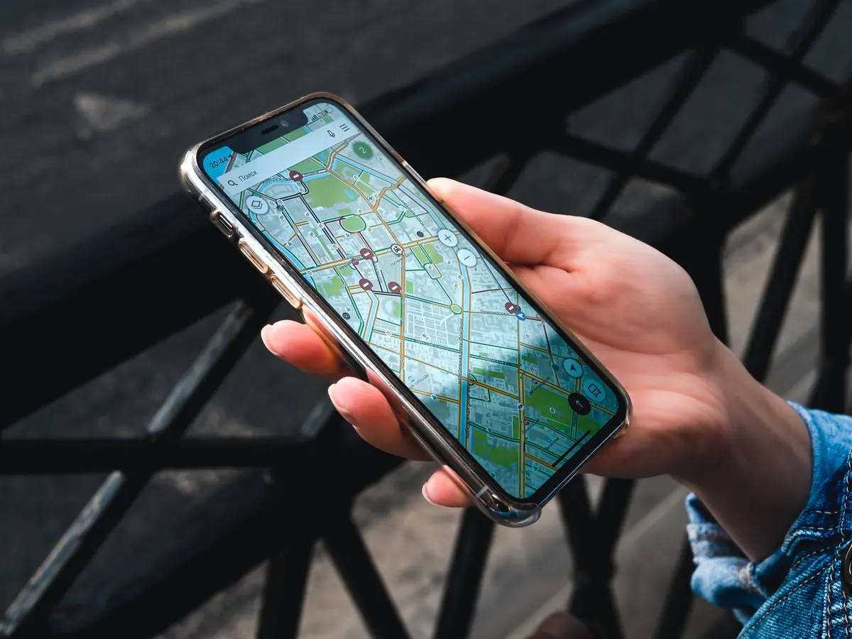 Hand holding a smartphone showing a city map with location pins, outdoors by a street railing