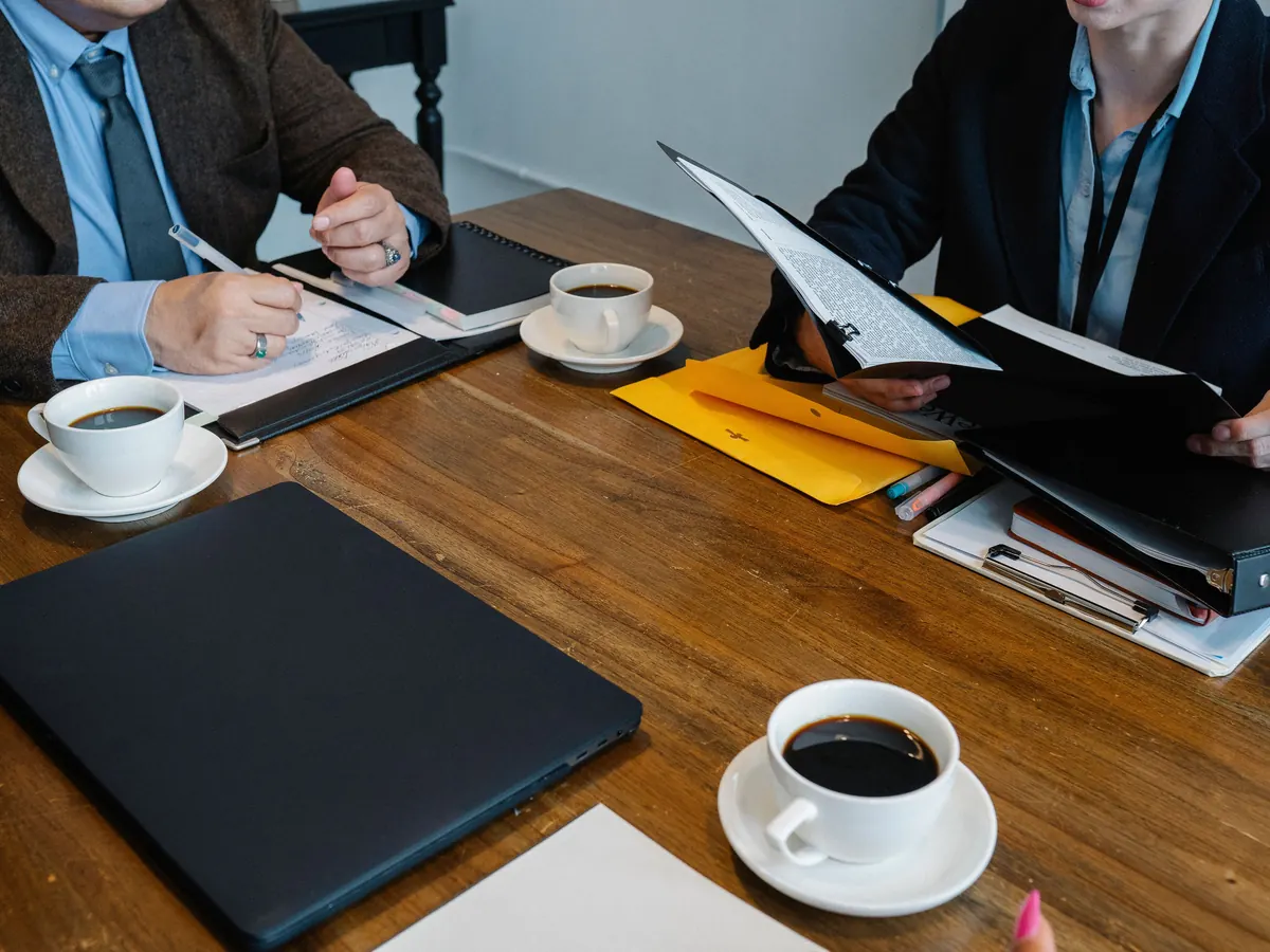 Choosing between SEO and website packages: colleagues reviewing documents and folders over coffee at a wooden meeting table