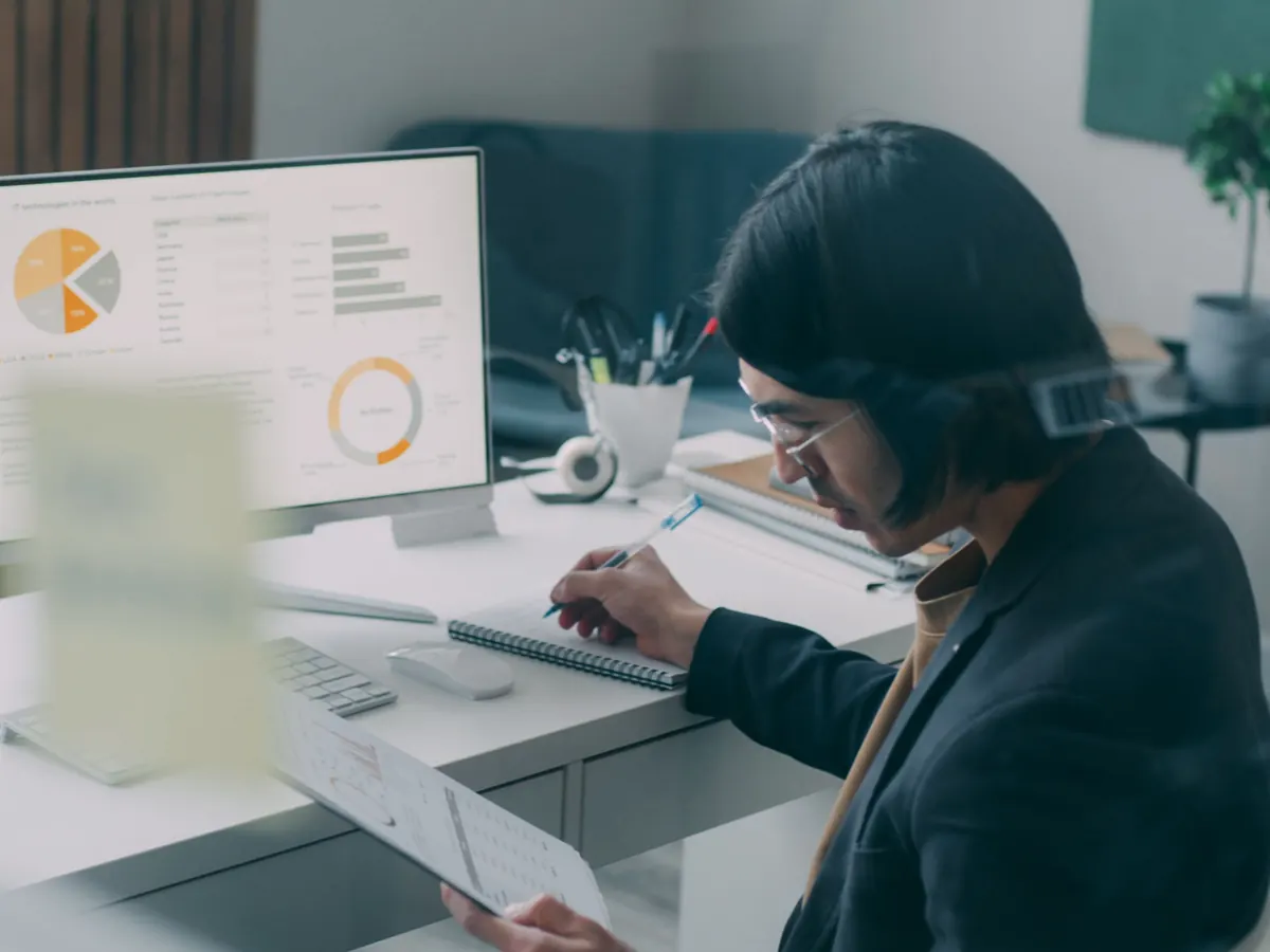SEO specialist taking notes while reviewing SEO services analytics charts on a desktop monitor