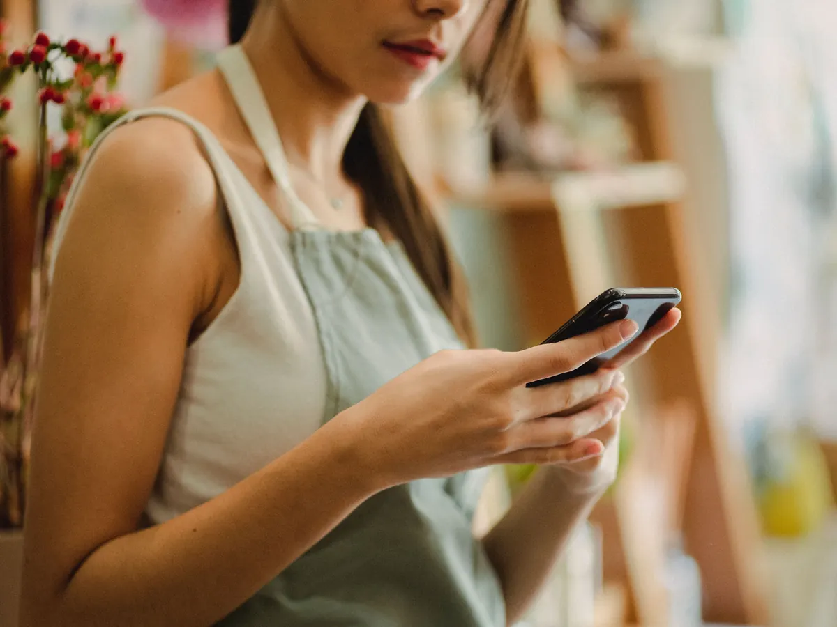 Florist in an apron checking her smartphone in a flower shop