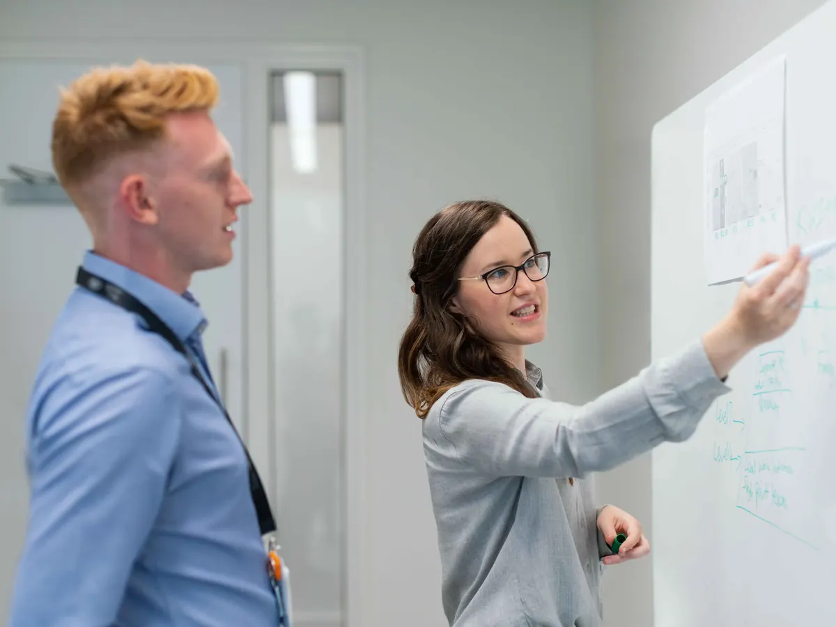Consultant explaining a plan on a whiteboard to a colleague in a bright office
