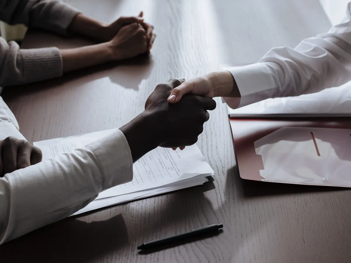 Handshake over printed contract papers at a meeting table, representing the working relationships behind client testimonials